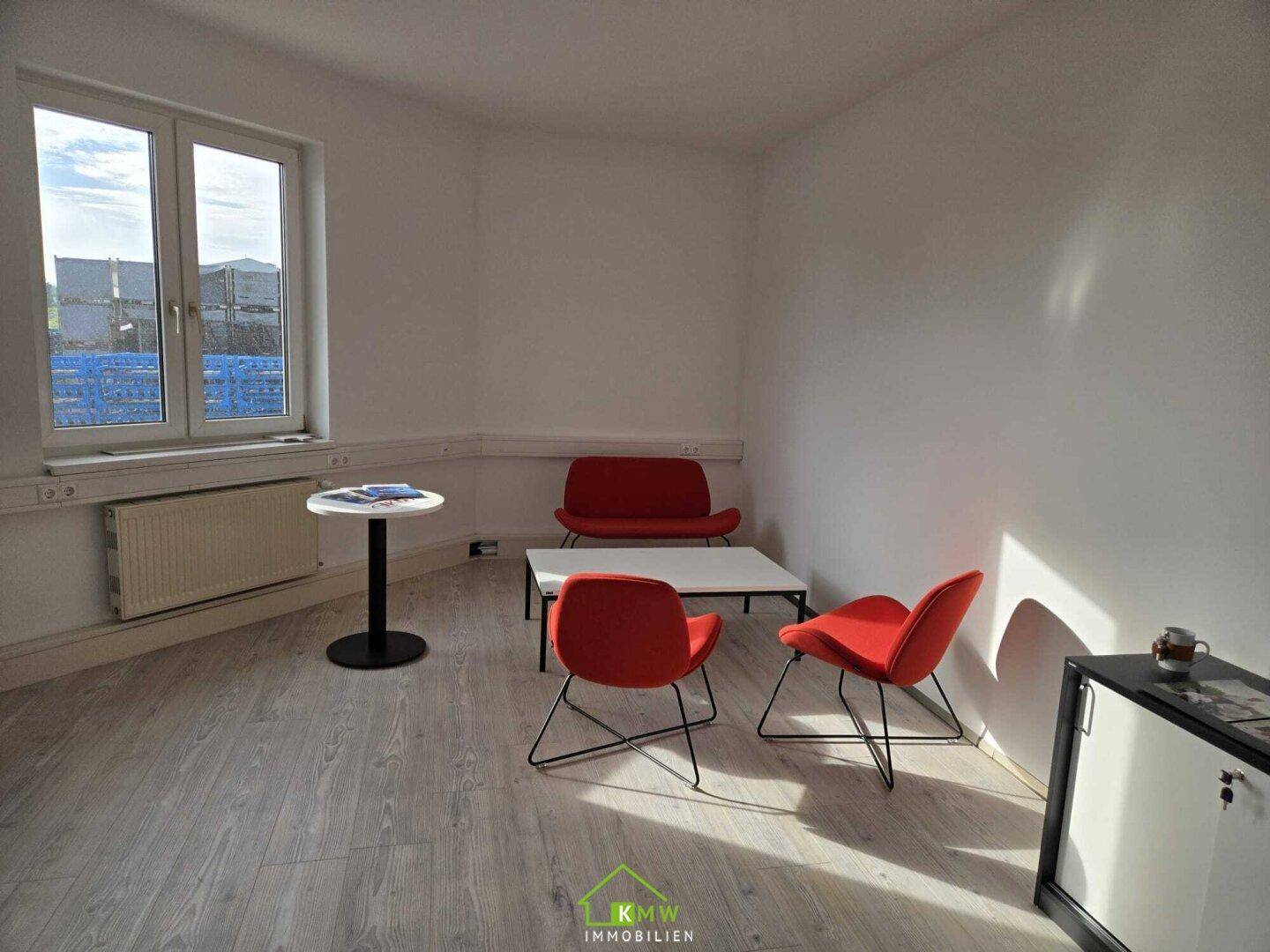 Gemütlicher Loungebereich mit roten Sesseln, kleinem Tisch und hellem Laminatboden.