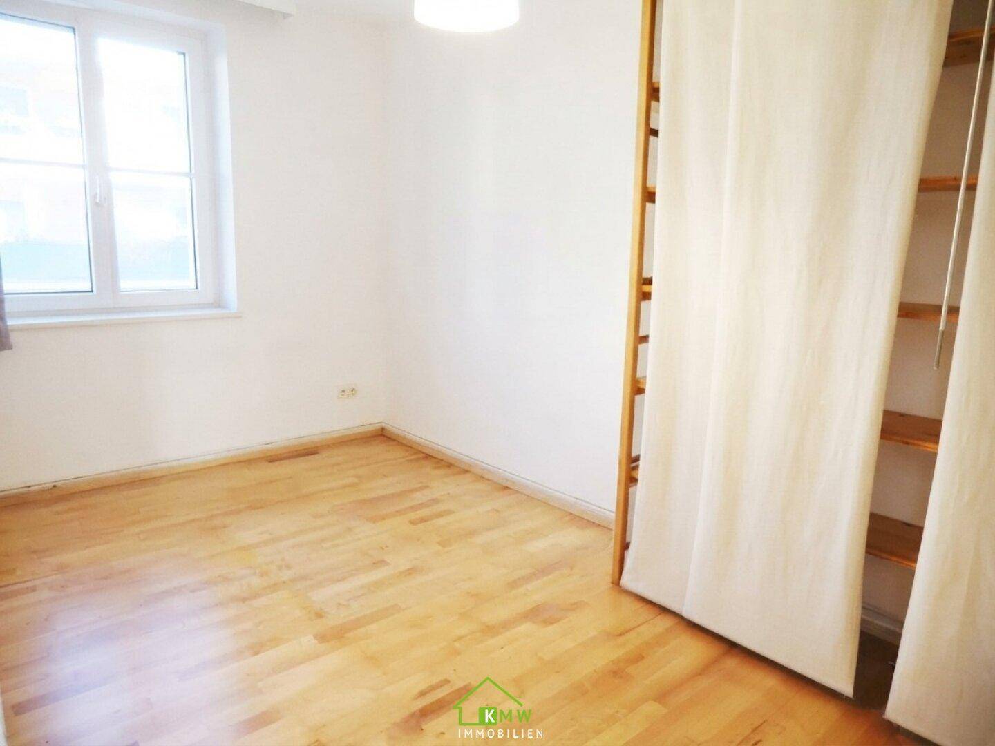 Helles Schlafzimmer mit Laminatboden und einem Fenster, das viel Tageslicht hereinlässt.