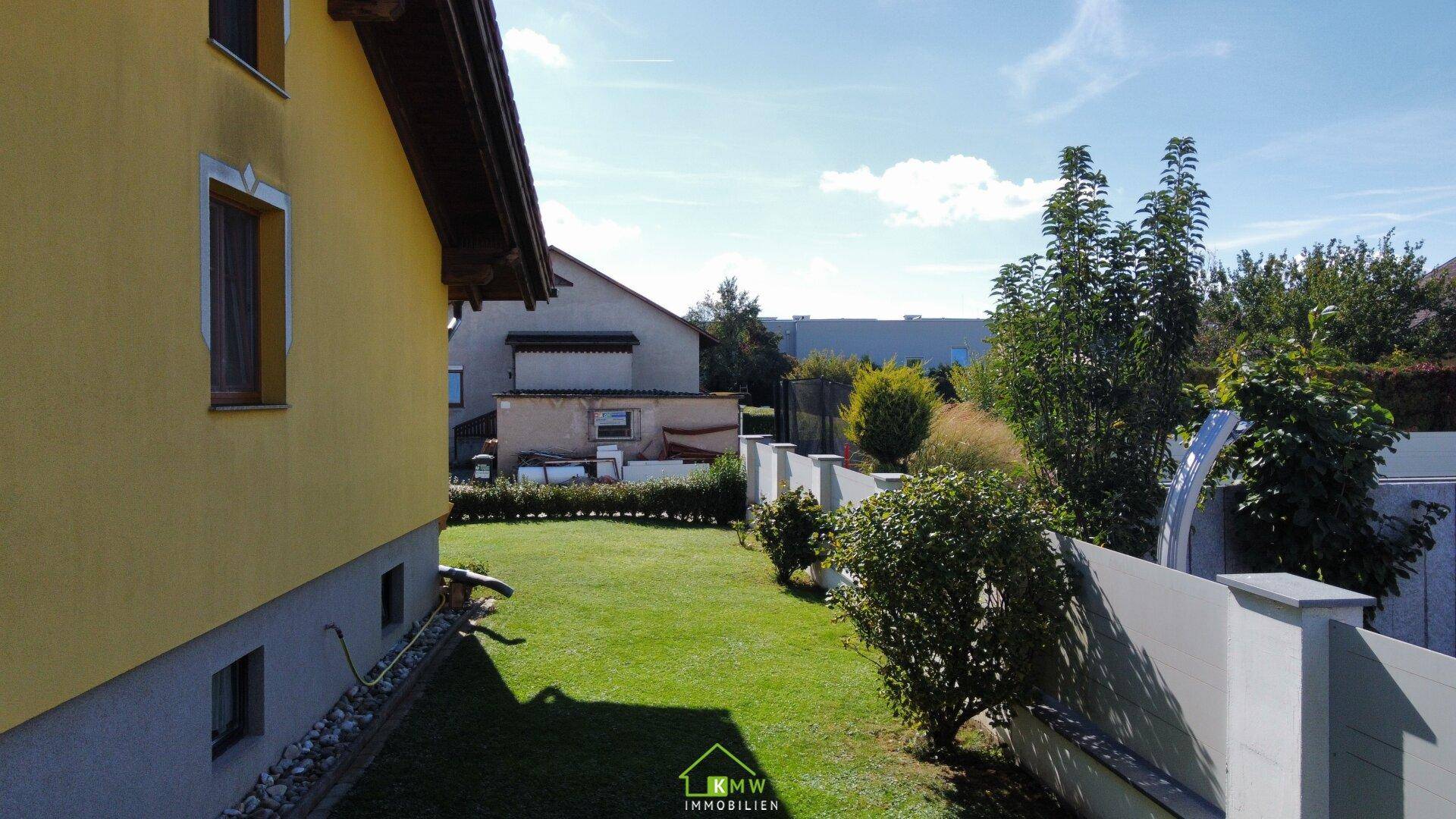 Seitlicher Gartenbereich mit Rasenfläche und Hecke unter blauem Himmel.
