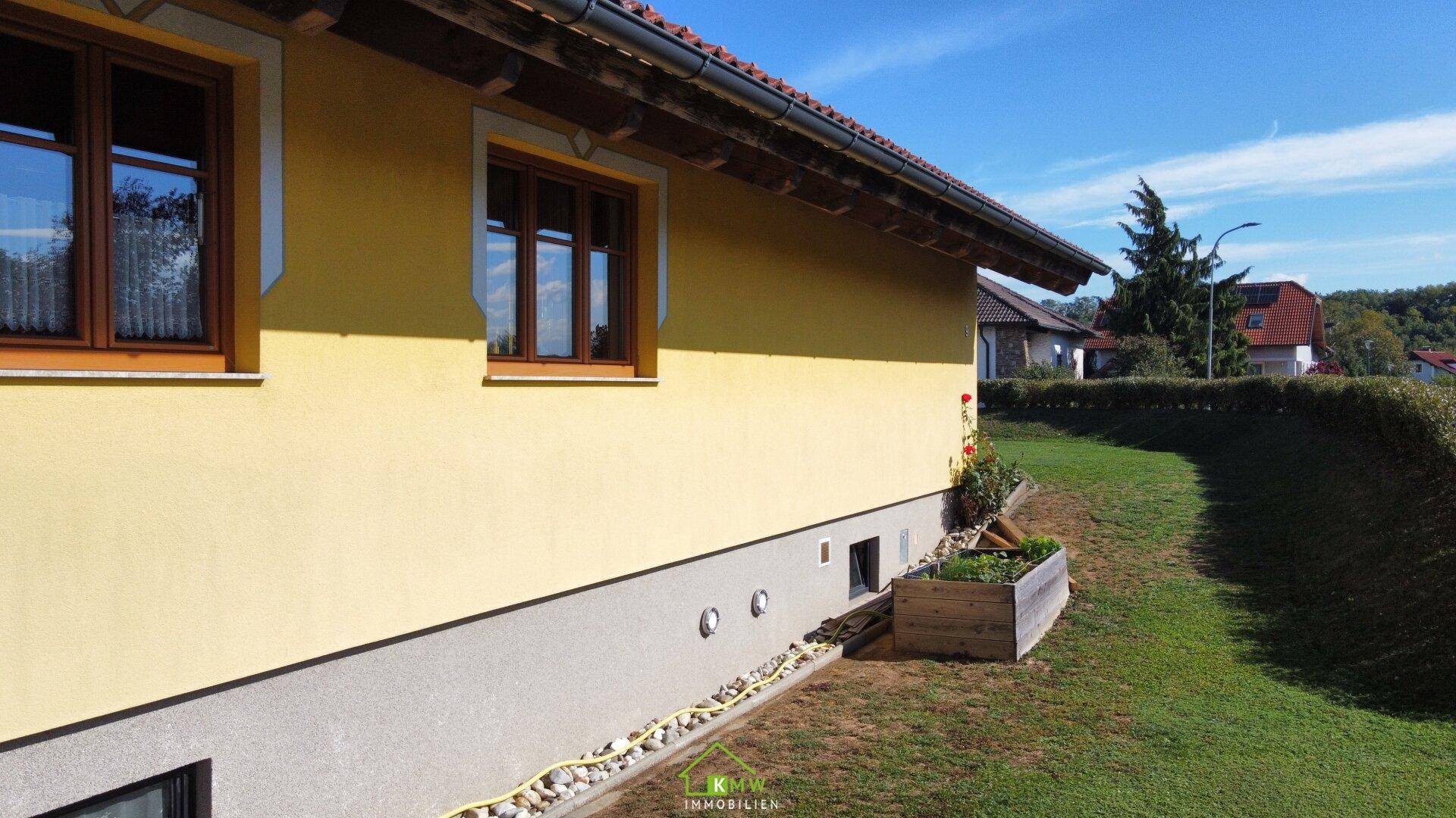 Seitenansicht des Hauses mit gelber Fassade, Holzfenstern und gepflegtem Garten.