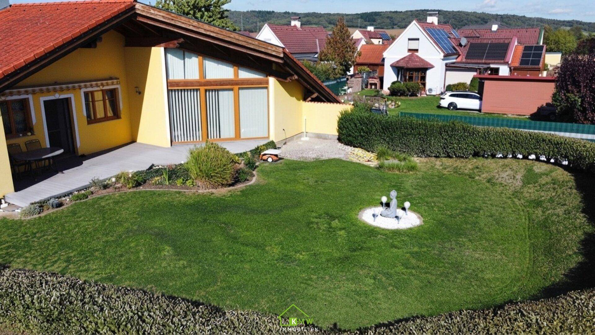 Weitläufiger Gartenbereich mit Rasenfläche und kleiner Terrasse am gelben Haus.