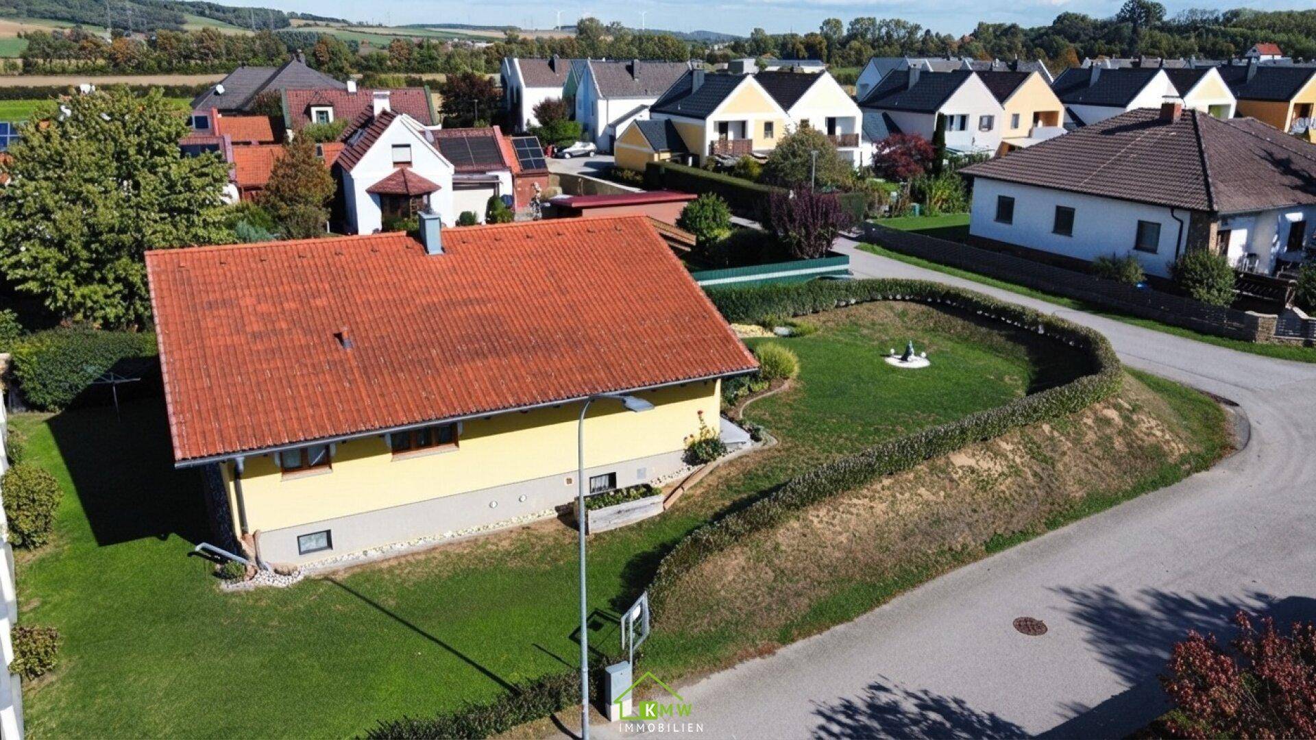 Überblick über das gelbe Einfamilienhaus mit Garten und die umliegende Wohnsiedlung.