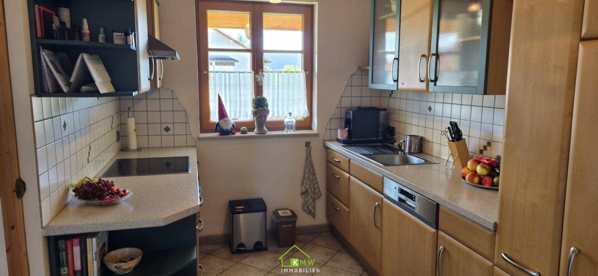 Gemütliche Küche mit Holzschränken, Fliesenboden und Fensterblick ins Grüne.