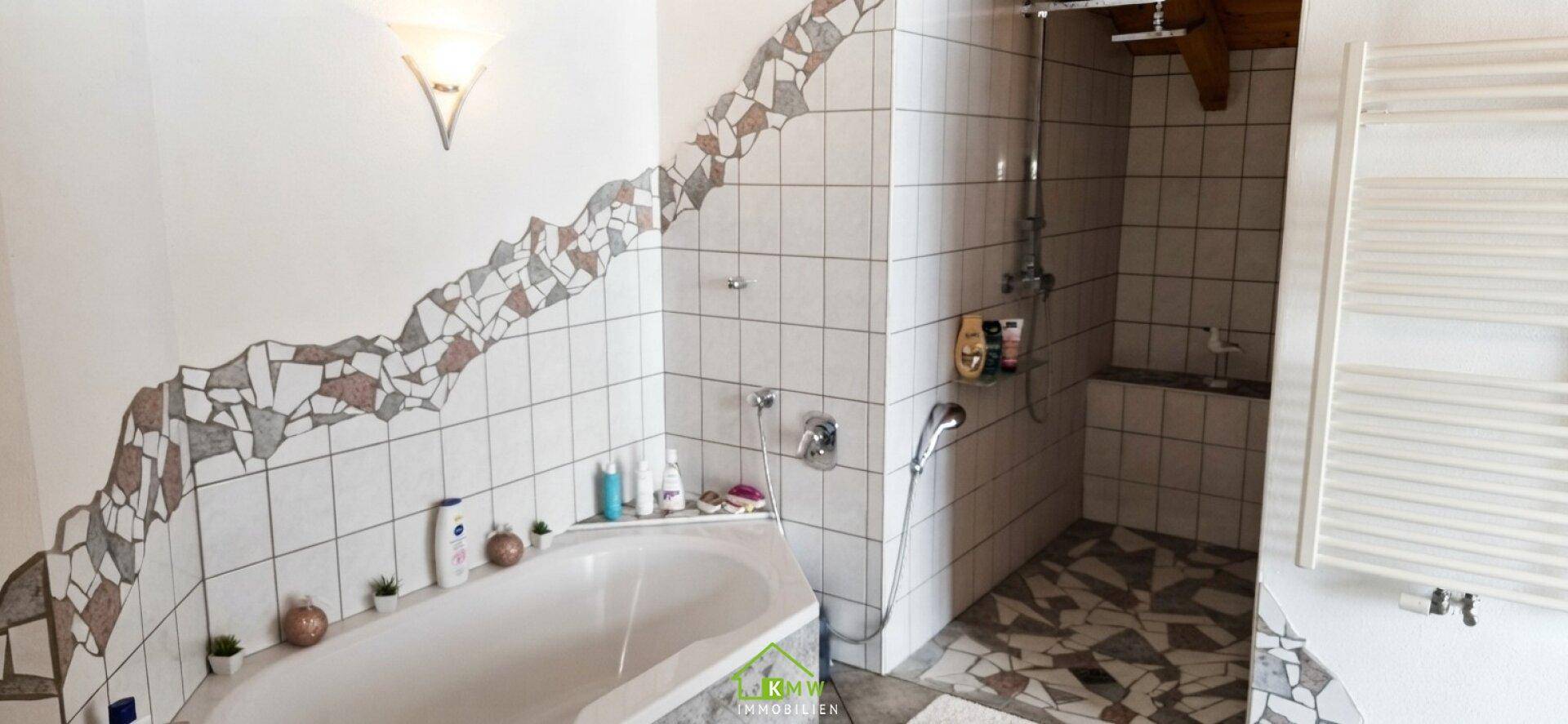 Badezimmer mit Badewanne, Dusche und dekorativen Fliesen in Weiß und Braun.