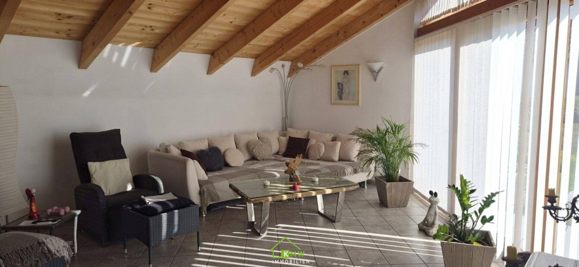 Geräumiges Wohnzimmer mit Holzbalkendecke, großer Couch und viel Tageslicht.