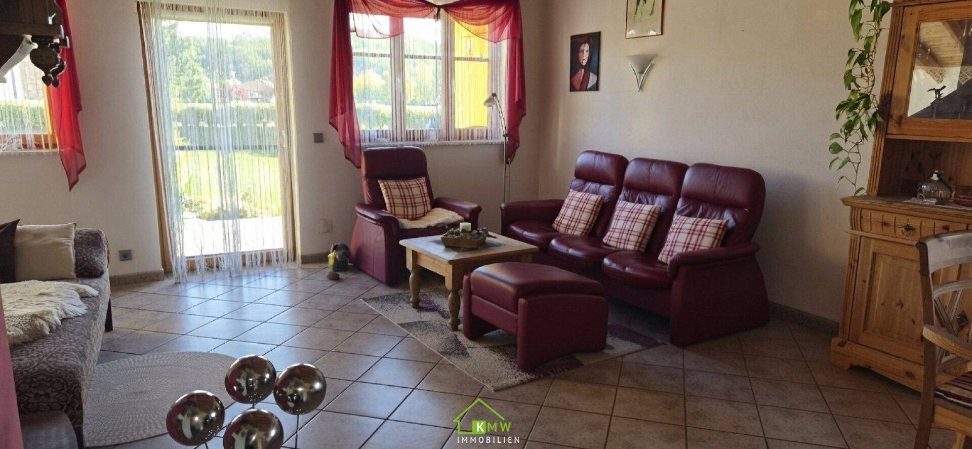 Gemütliches Wohnzimmer mit Ledersofa, Fliesenboden und Blick in den Garten.