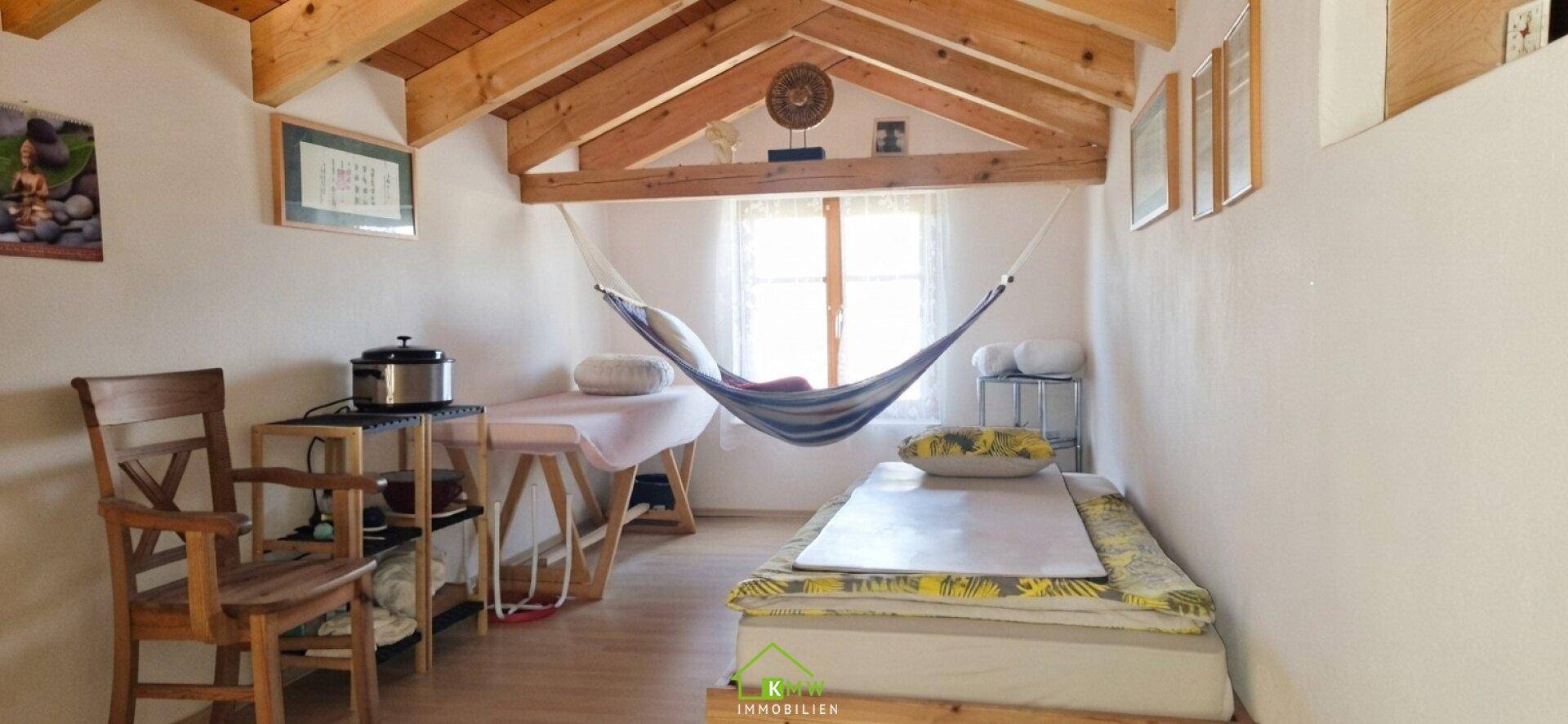 Schlafzimmer mit Holzbalkendecke, Hängematte und einfacher Einrichtung.