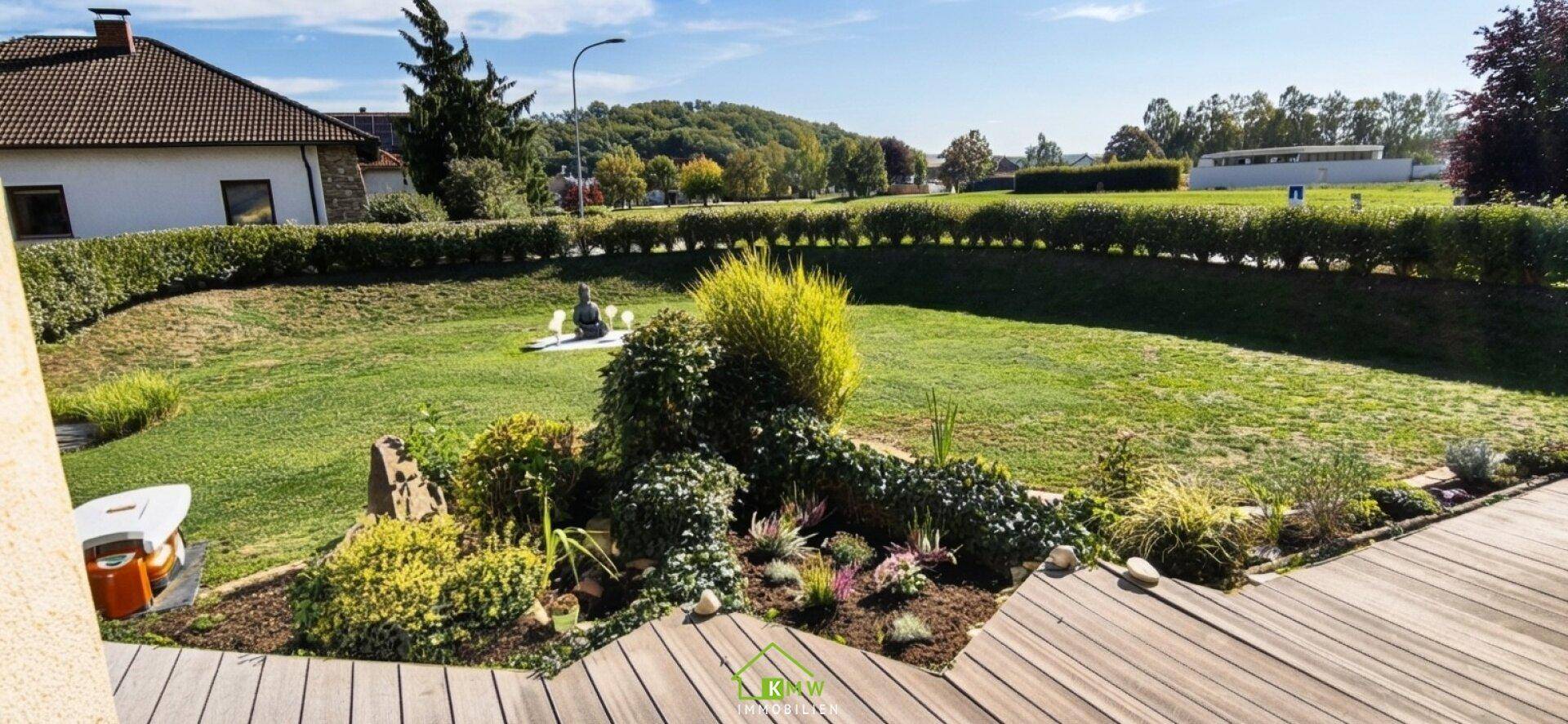 Großer Garten mit Holzterrasse, Rasenfläche und vielfältiger Bepflanzung.