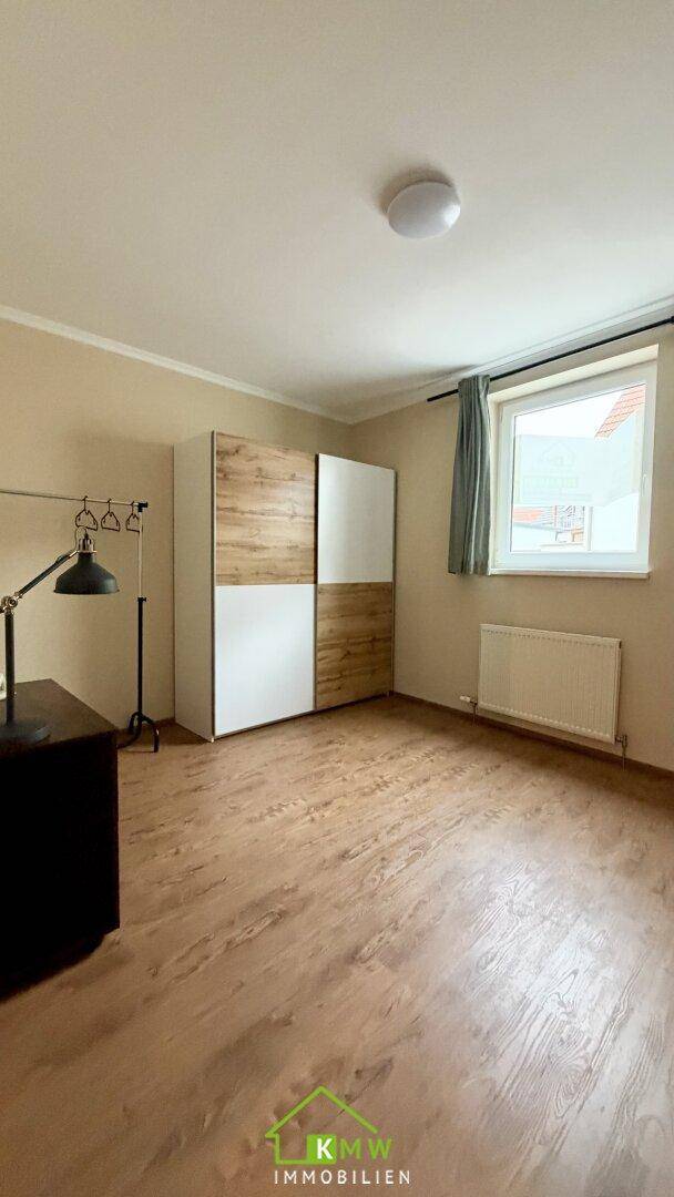 Schlafzimmer mit Holzboden, großem Fenster und modernem Kleiderschrank.