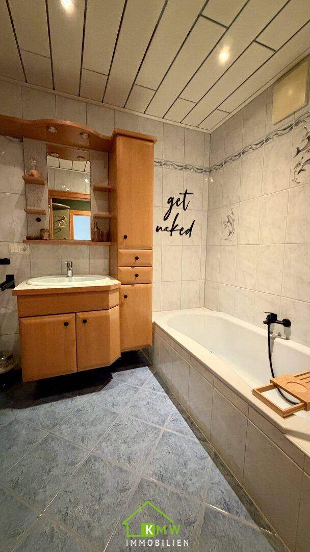Badezimmer mit Badewanne, Waschbecken und Holzschrank.