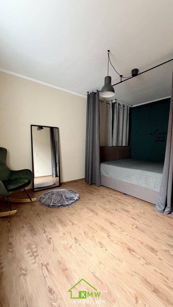 Gemütliches Schlafzimmer mit Holzboden, Spiegel und Vorhängen am Bettbereich.