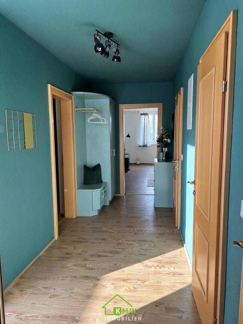 Heller Flur mit blauen Wänden, Holzboden und Garderobenbereich.