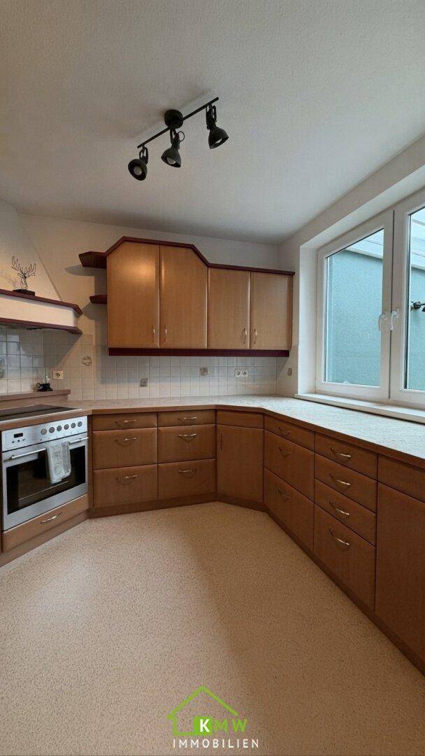 Funktionale Küche mit Holzschränken, Einbaugeräten und Fenster.