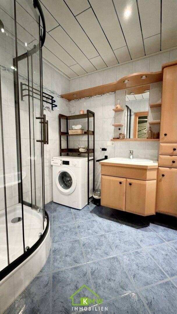 Badezimmer mit Dusche, Waschmaschine und blauen Fliesen.