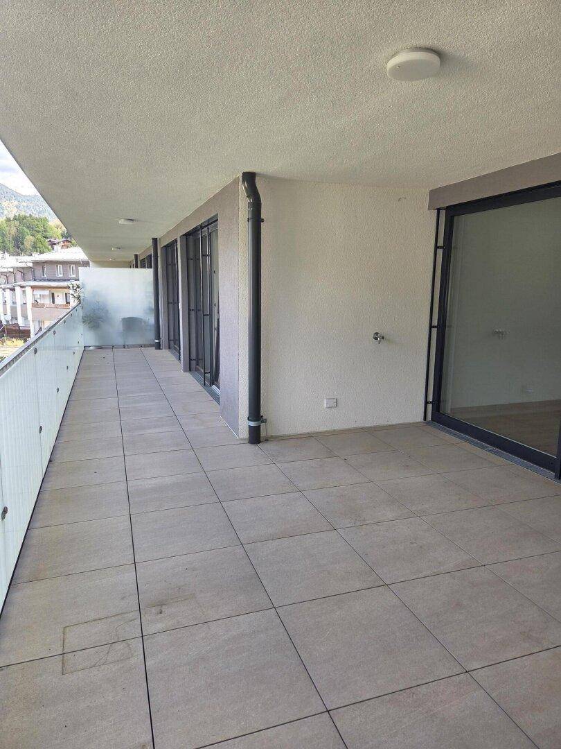 Geräumiger Balkon mit Fliesenboden, Glasgeländer und Blick auf die umliegende Berglandschaft.