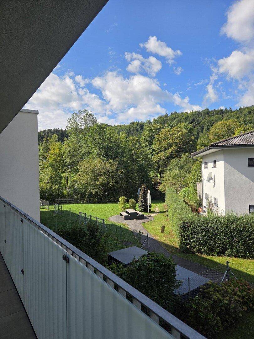 Blick vom Balkon auf einen gepflegten Gartenbereich mit Rasenfläche und Bäumen.