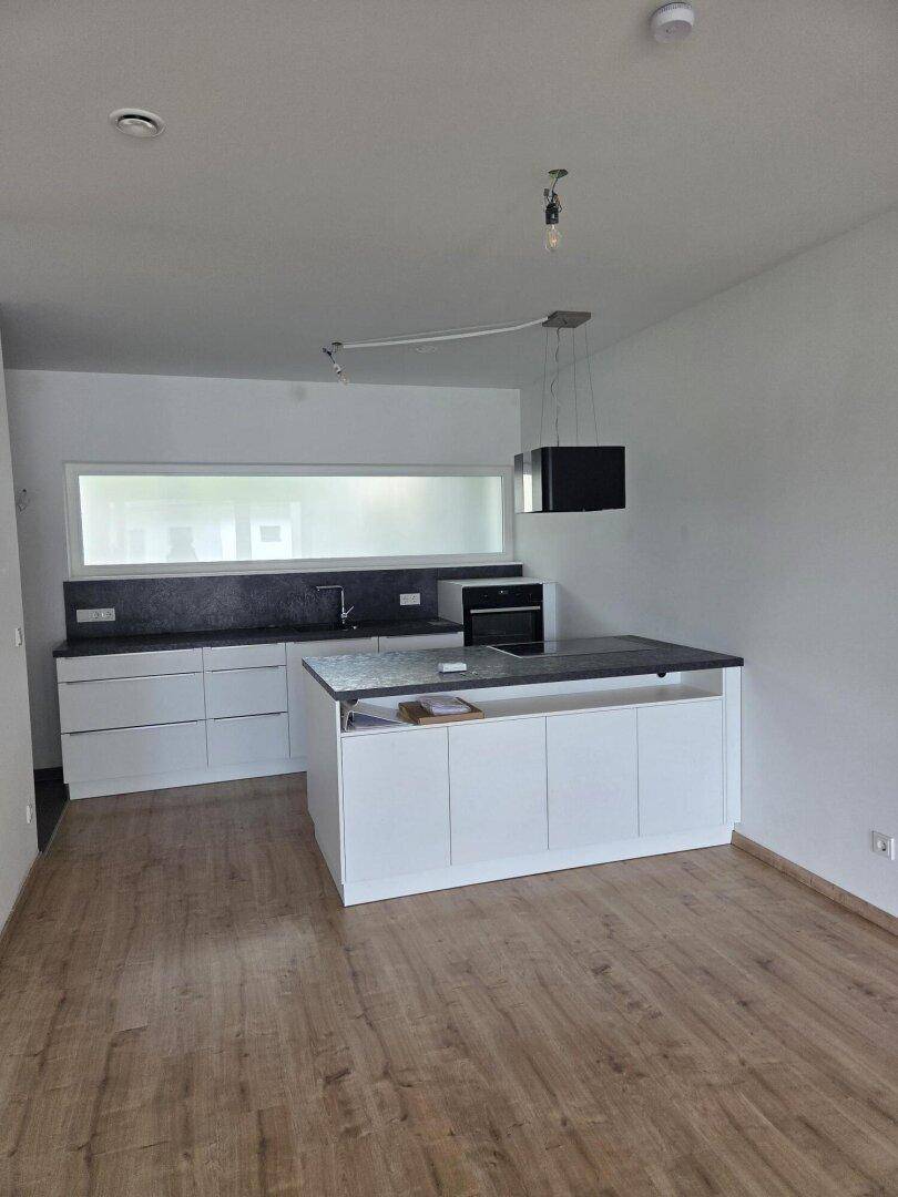 Moderne Küche mit weißen Schränken, Kücheninsel, dunklen Arbeitsplatten und Laminatboden.