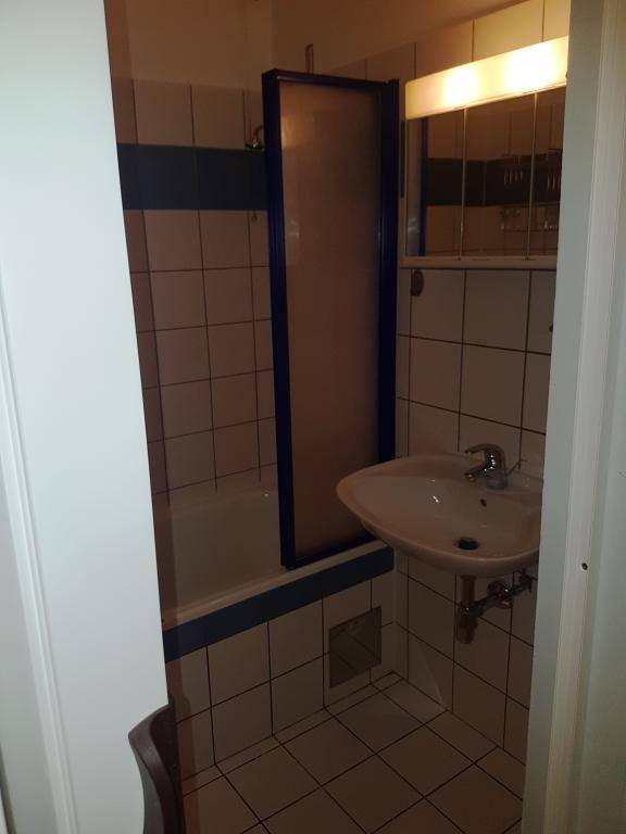 Badezimmer mit Waschbecken, Spiegelschrank und Badewanne mit Duschabtrennung in Blau-Weiß.