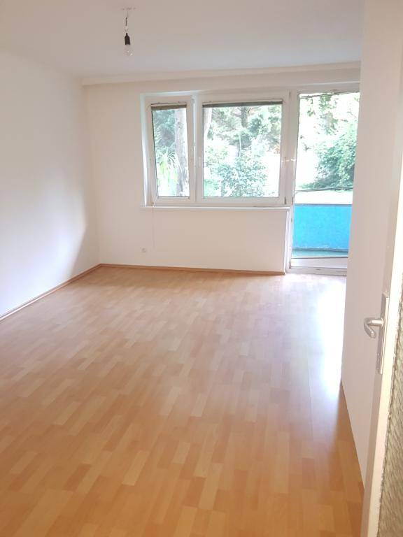 Geräumiger, heller Wohnraum mit Holzparkettboden, großen Fenstern und Zugang zum Garten.