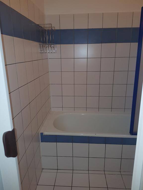Nahaufnahme der Badewanne mit blauen und weißen Fliesen, inklusive Duschabtrennung.