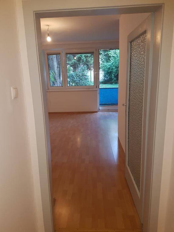 Heller Wohnraum mit Holzparkettboden und Blick ins Grüne, mit Zugang zum Außenbereich.
