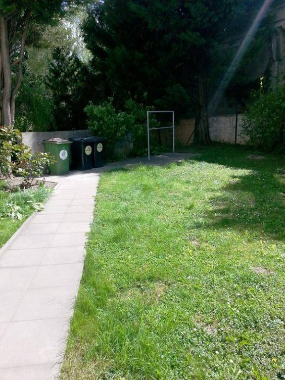Gepflegter Gartenbereich mit Rasenfläche, Bäumen und einem gepflasterten Weg.