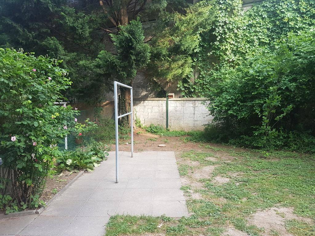 Ruhiger Gartenbereich mit Rasenfläche, gepflastertem Weg und üppiger Bepflanzung.