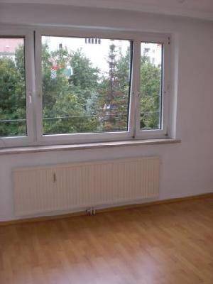 Heller Wohnraum mit Parkettboden, großem Fenster und einem Heizkörper unterhalb der Fensterbank.
