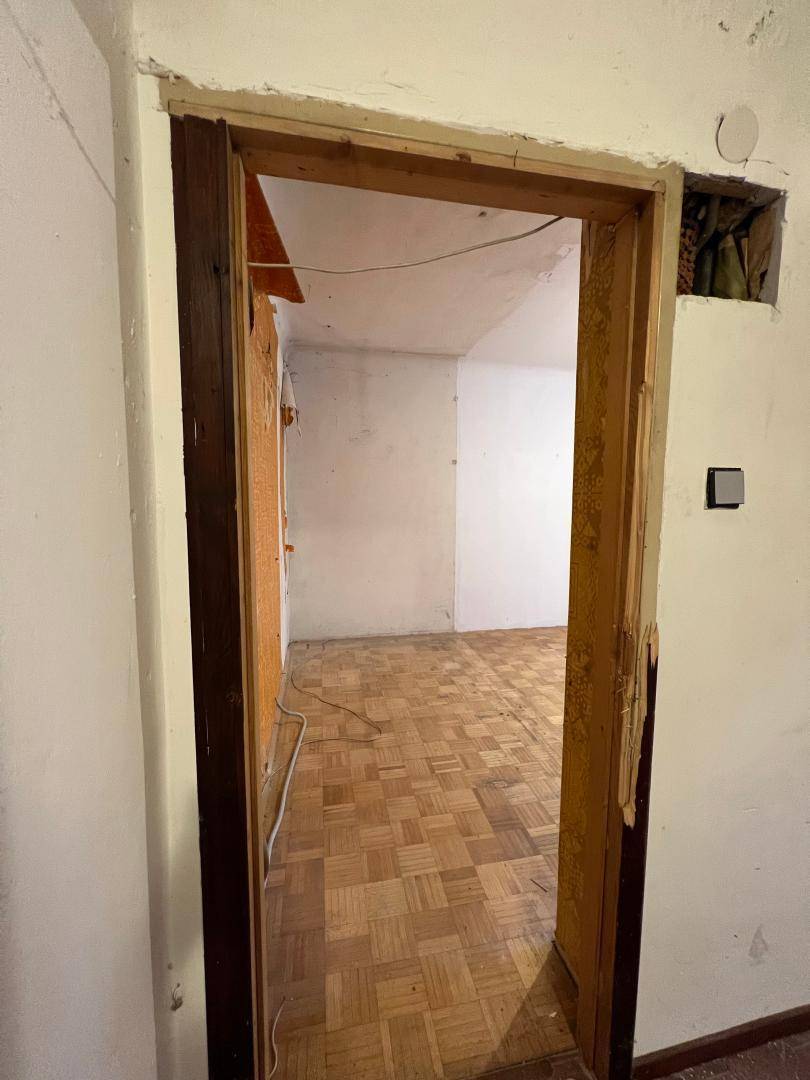 Türrahmen führt in einen leeren Raum mit Fischgrätparkett und weißen Wänden, der renoviert werden muss.