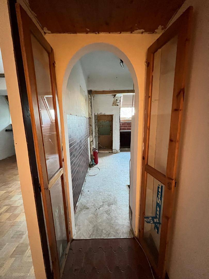 Gewölbter Durchgang mit verglasten Holztüren führt in einen Flur mit gefliesten Wänden und Boden.