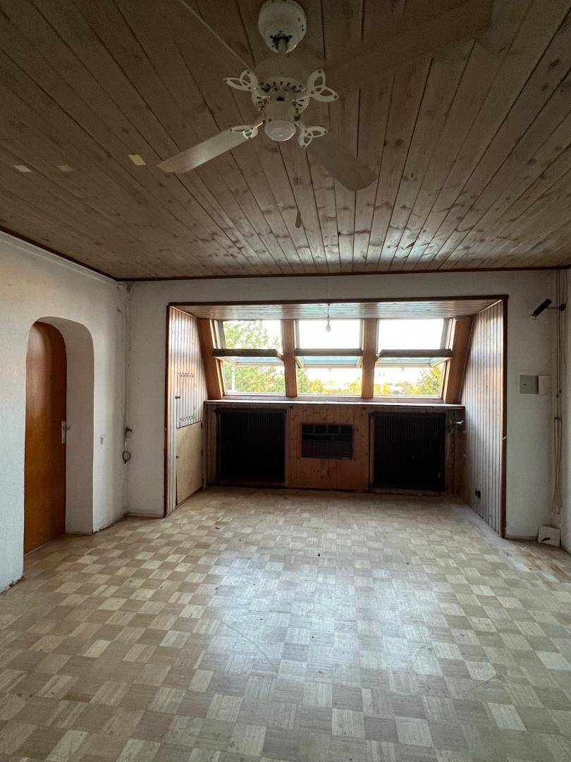 Heller Wohnraum mit Holzdecke, Parkettboden und einem Deckenventilator über der Fensterfront.