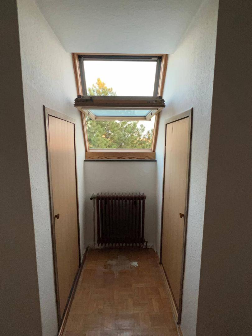 Schmaler Flur mit Parkettboden, Heizkörper und einem Dachfenster, flankiert von zwei Holztüren.
