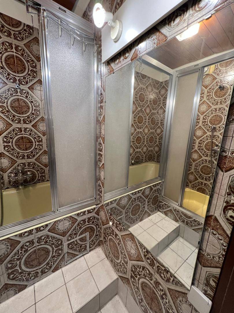 Duschbereich im Badezimmer mit gemusterten Fliesen und einer Duschkabine mit Schiebetüren.