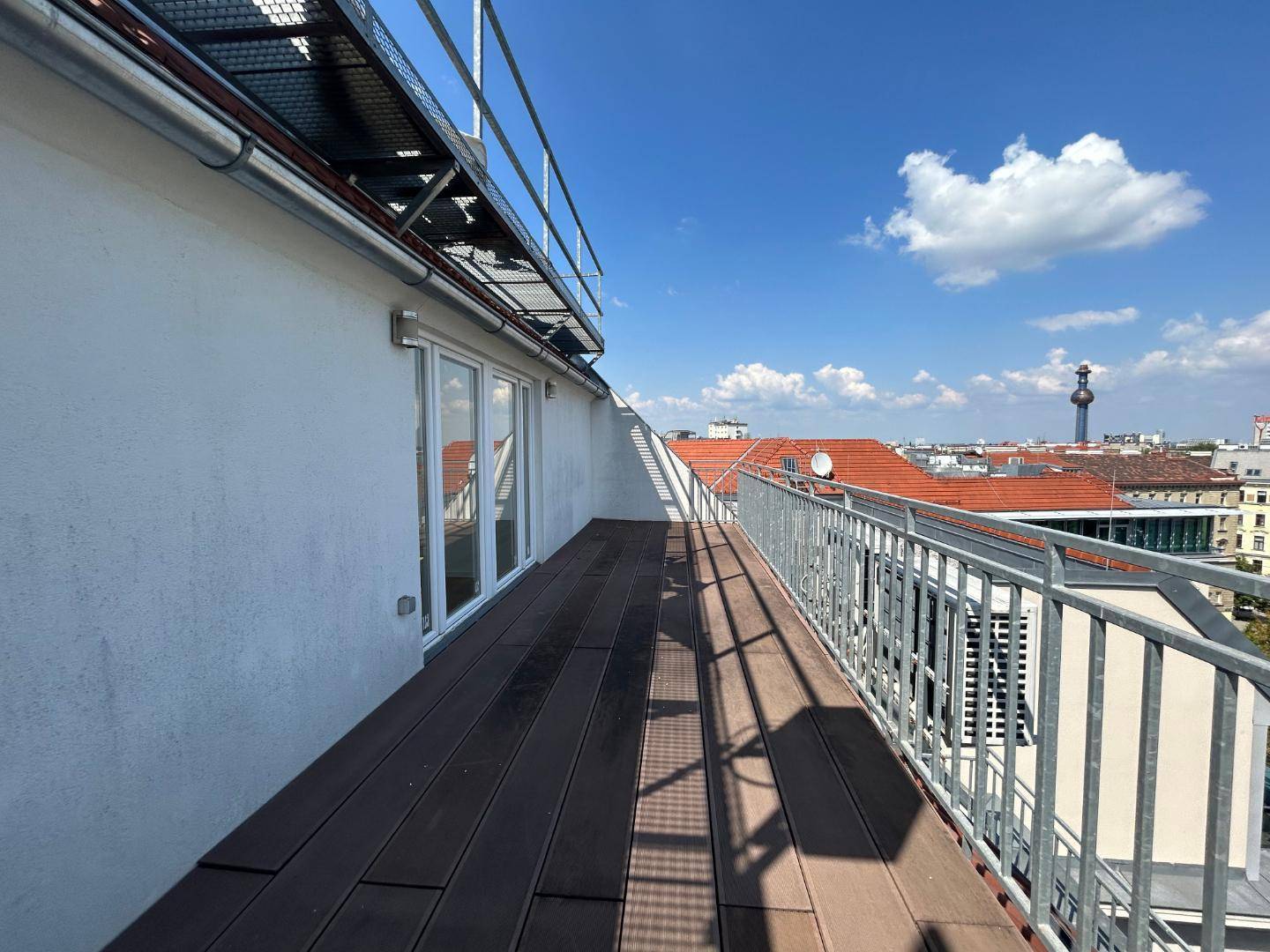 Lange Dachterrasse mit Holzdielen und Metallgeländer bietet einen weiten Blick über die Stadt.