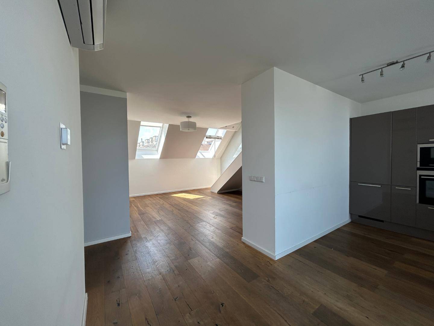 Offener Wohnbereich mit Holzdielenboden, schrägen Decken, Dachfenstern und integrierter Klimaanlage.