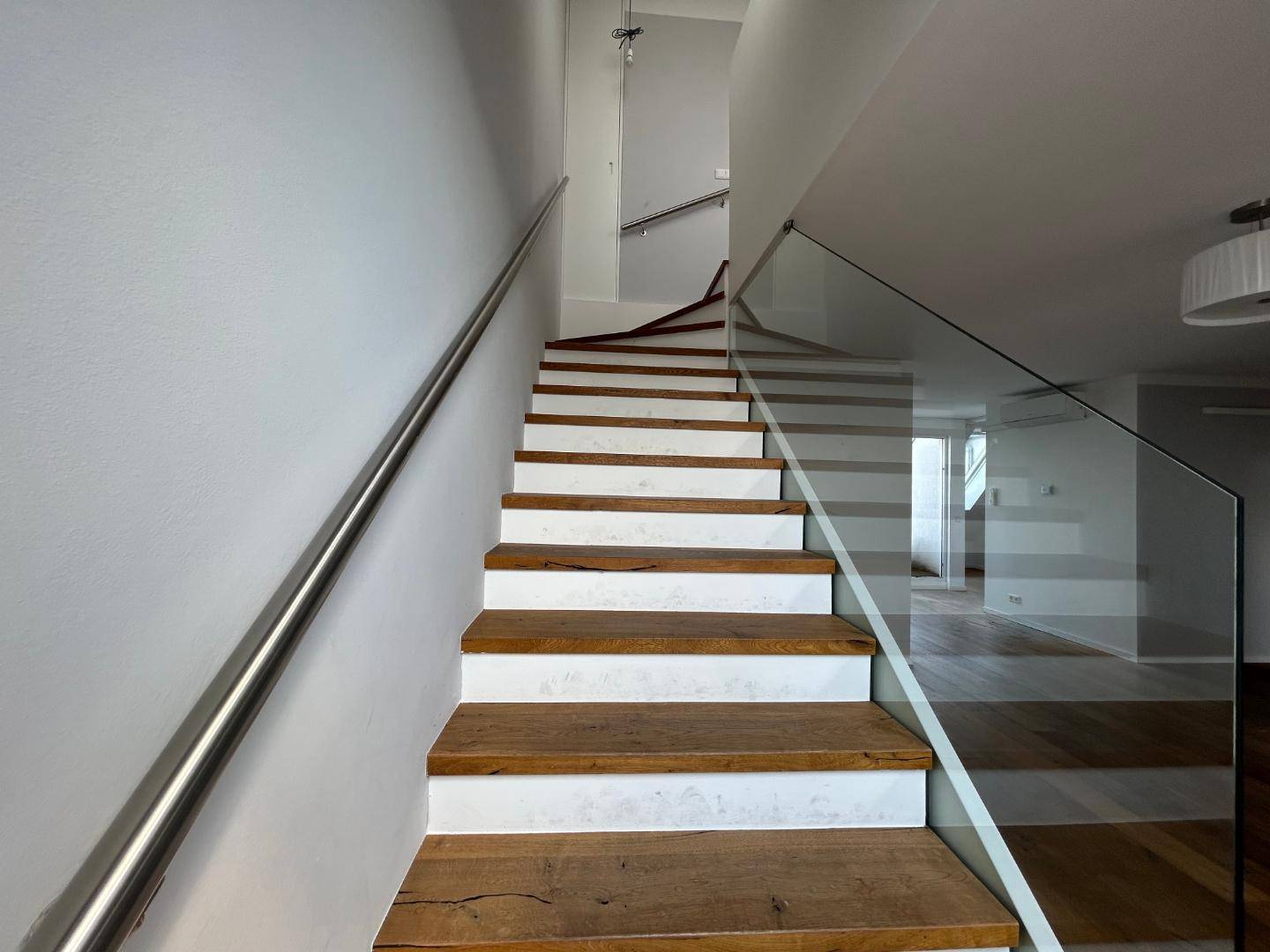 Blick nach oben auf die elegante Holztreppe mit Glasgeländer und Edelstahlhandlauf.