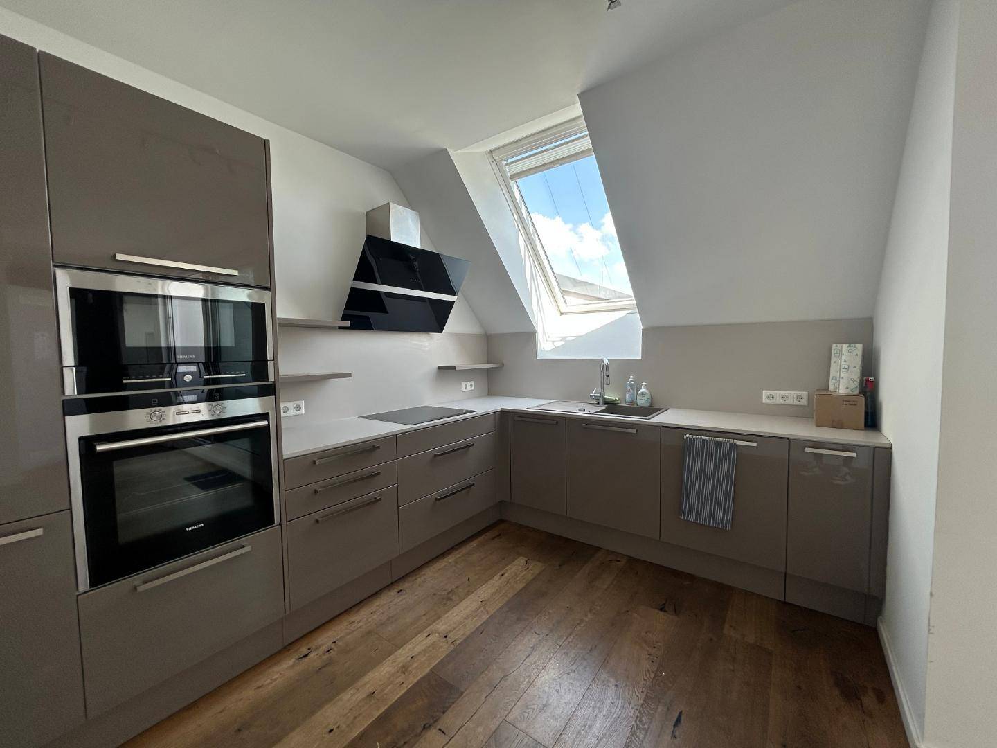 Moderne Einbauküche mit grauen Schränken, integrierten Geräten, Induktionskochfeld und Dachfenster.