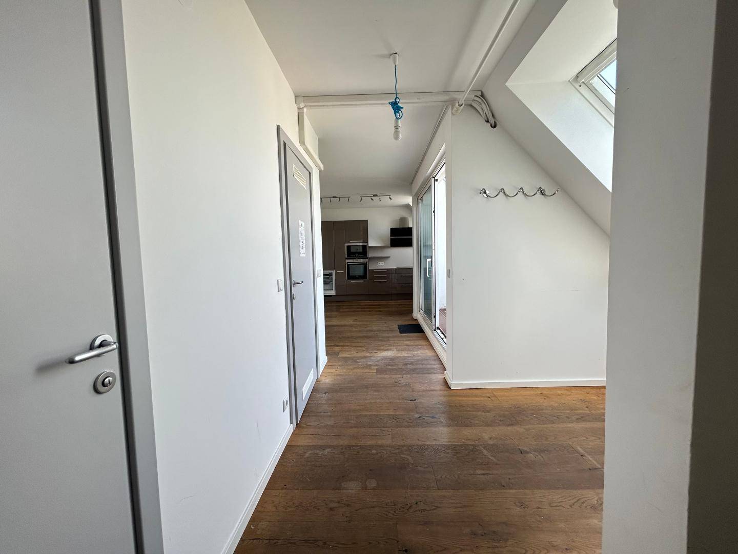 Übergangsbereich mit Holzdielenboden, weißen Wänden und Blick in eine moderne Küche im Dachgeschoss.