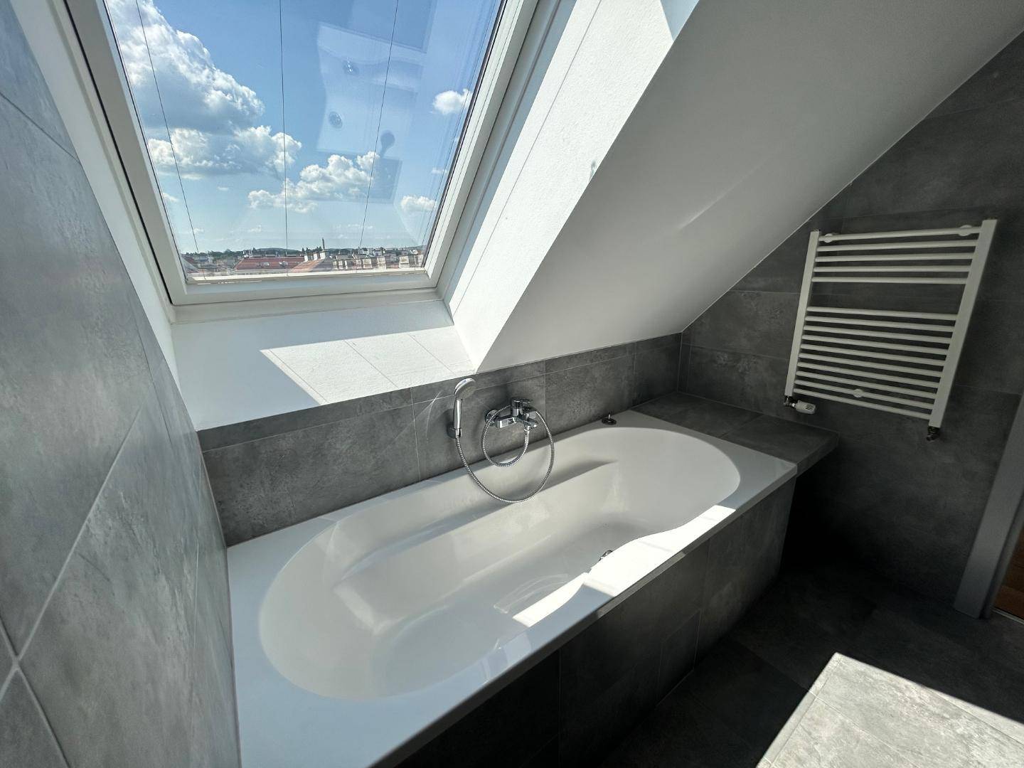 Badewanne unter großem Dachfenster mit Blick auf die Stadt und beheiztem Handtuchhalter.