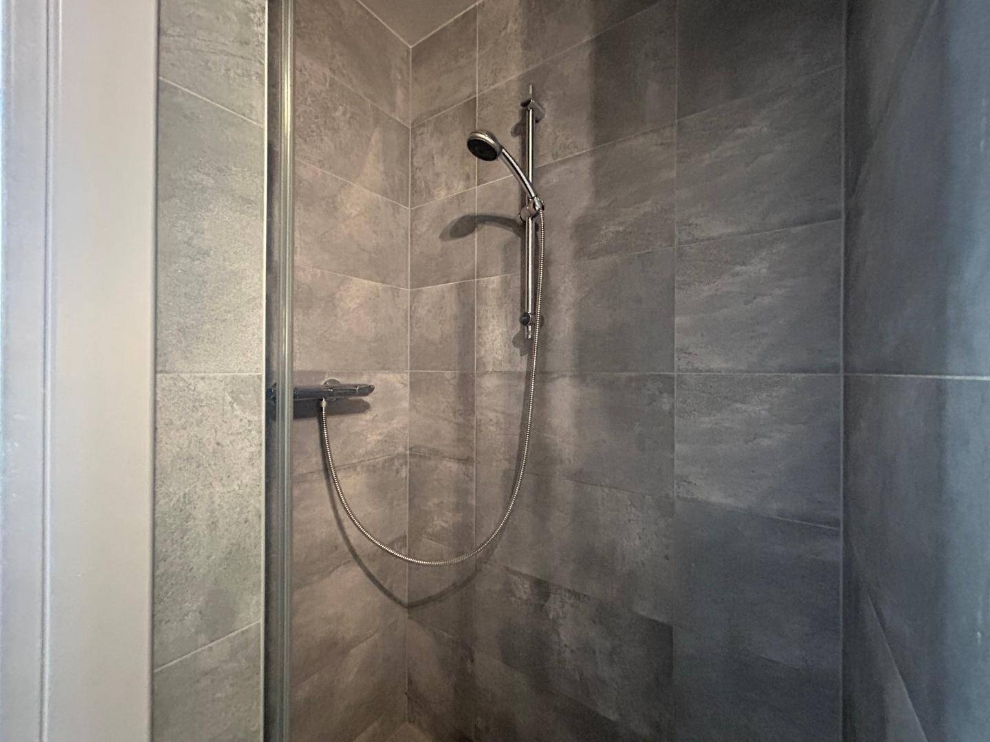 Detailansicht der Duscharmatur und der modernen grauen Fliesen in der begehbaren Dusche.