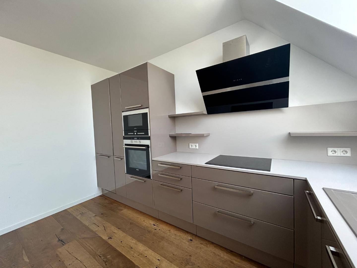 Detailansicht der modernen Küche mit grauen Hochglanzfronten, integriertem Backofen und Induktionskochfeld.