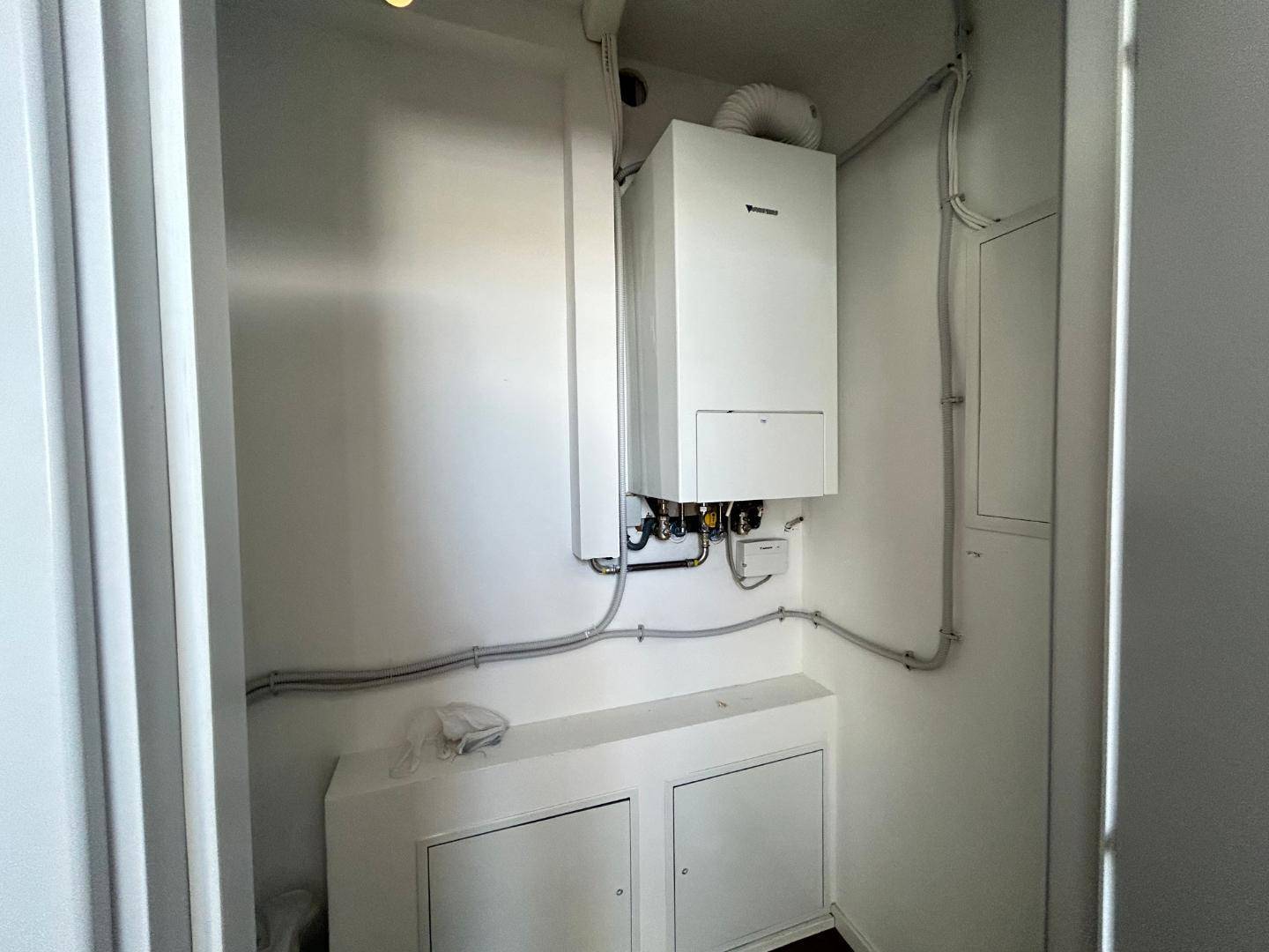 Kleiner Hauswirtschaftsraum mit Gastherme, weißen Wänden und sichtbaren Installationen.