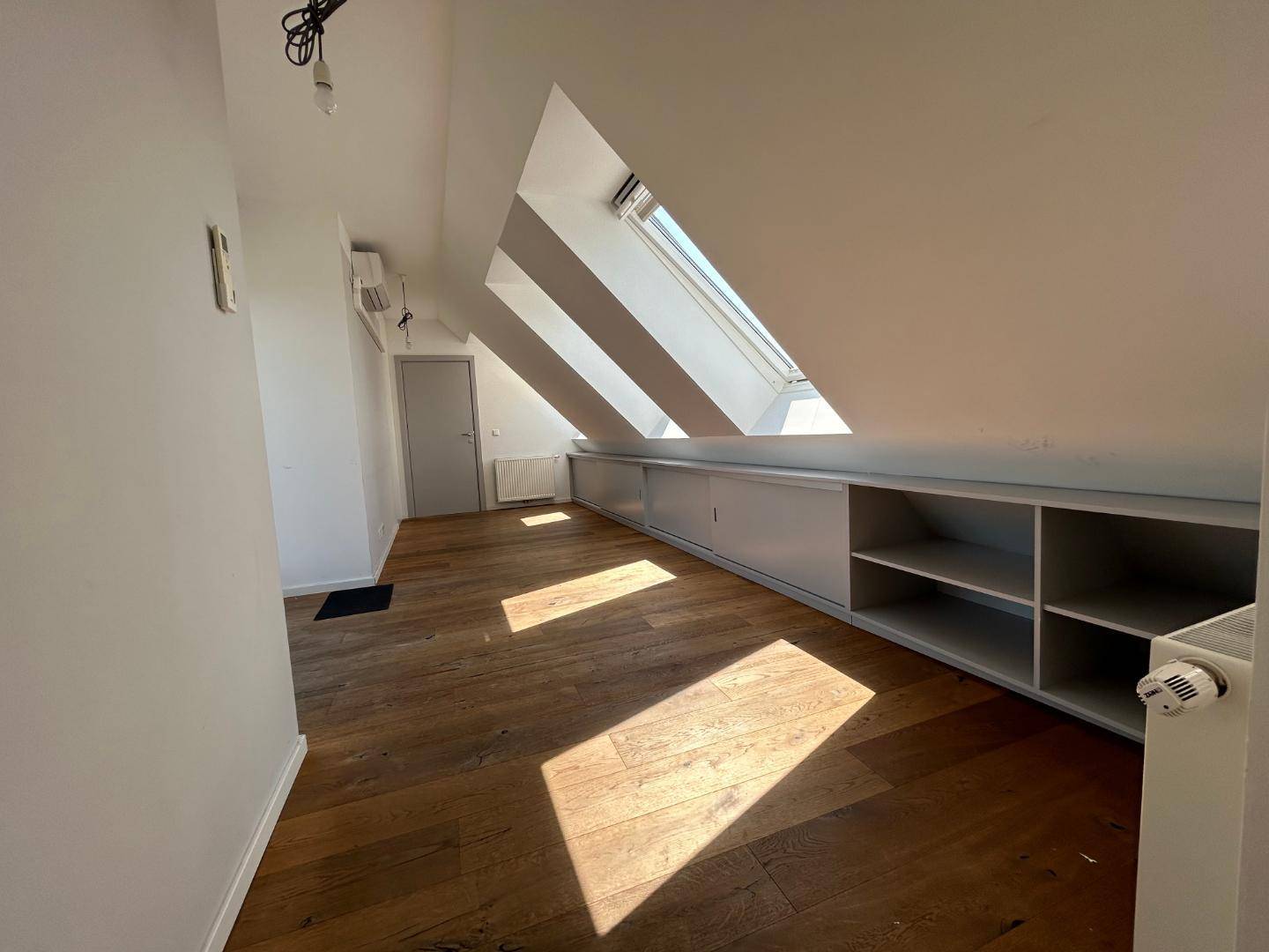 Heller Raum mit Holzdielenboden, schrägen Decken, mehreren Dachfenstern und integrierten Stauschränken.
