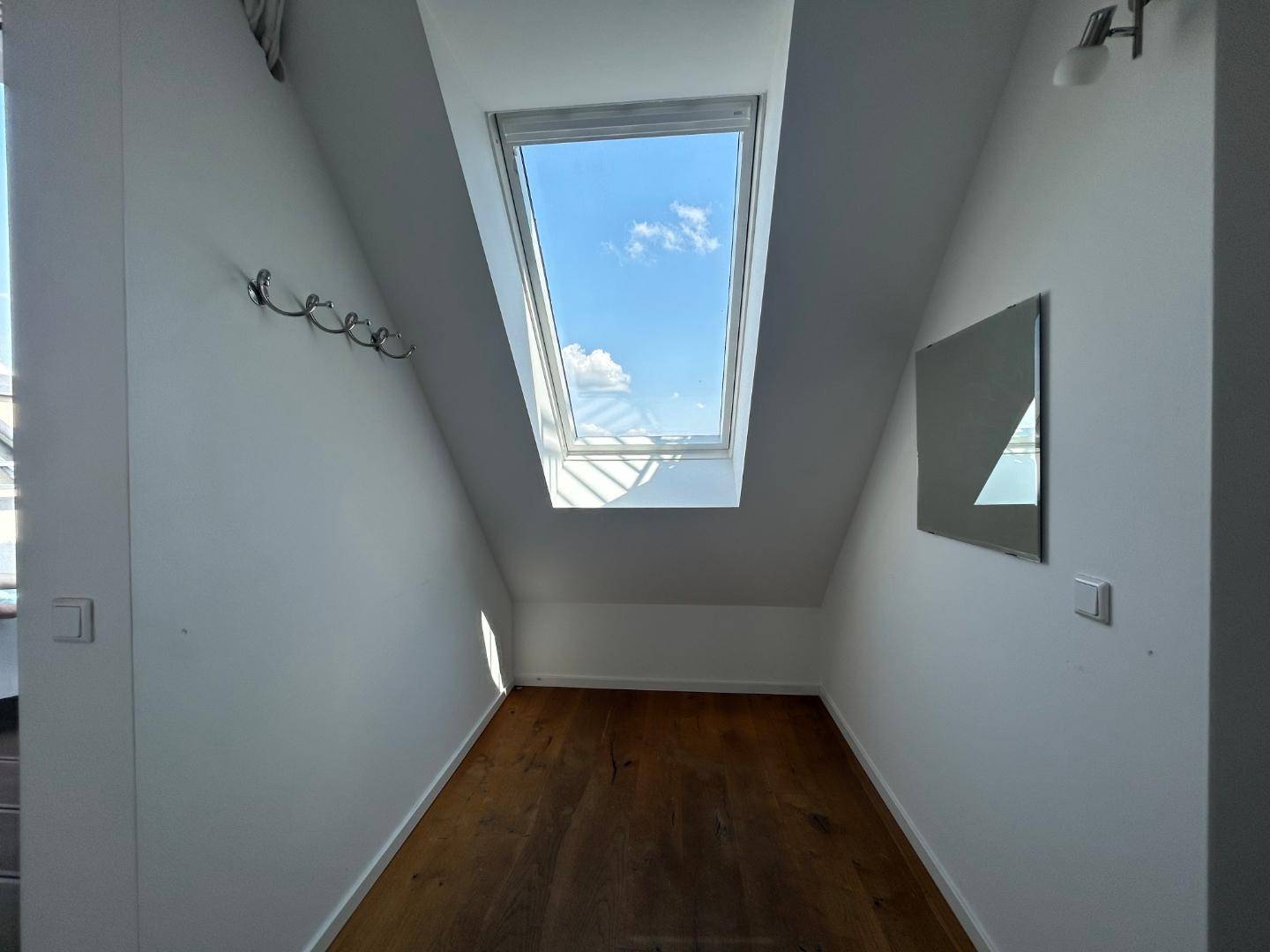 Heller Nischenbereich mit Holzdielenboden, schrägen Wänden und einem großen Dachfenster für viel Tageslicht.