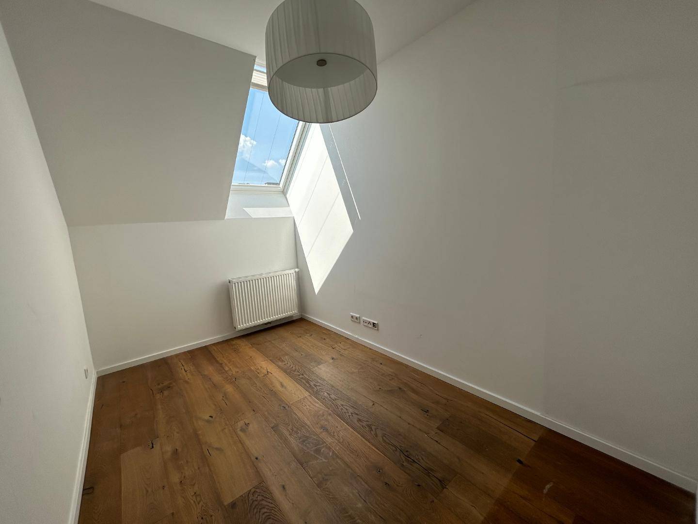 Helles Schlafzimmer mit Holzdielenboden, weißen Wänden, schräger Decke und einem großen Dachfenster.