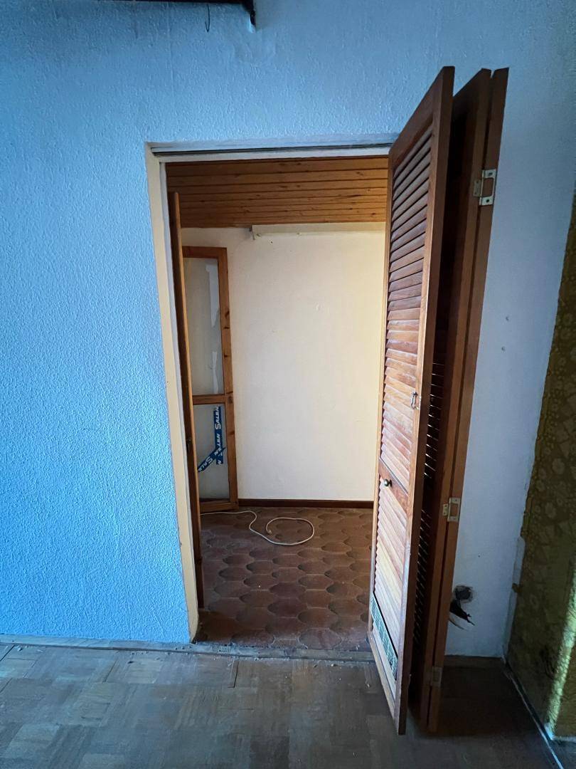 Tür mit Lamellen führt in einen Raum mit gemusterten Bodenfliesen und blauen Wänden.