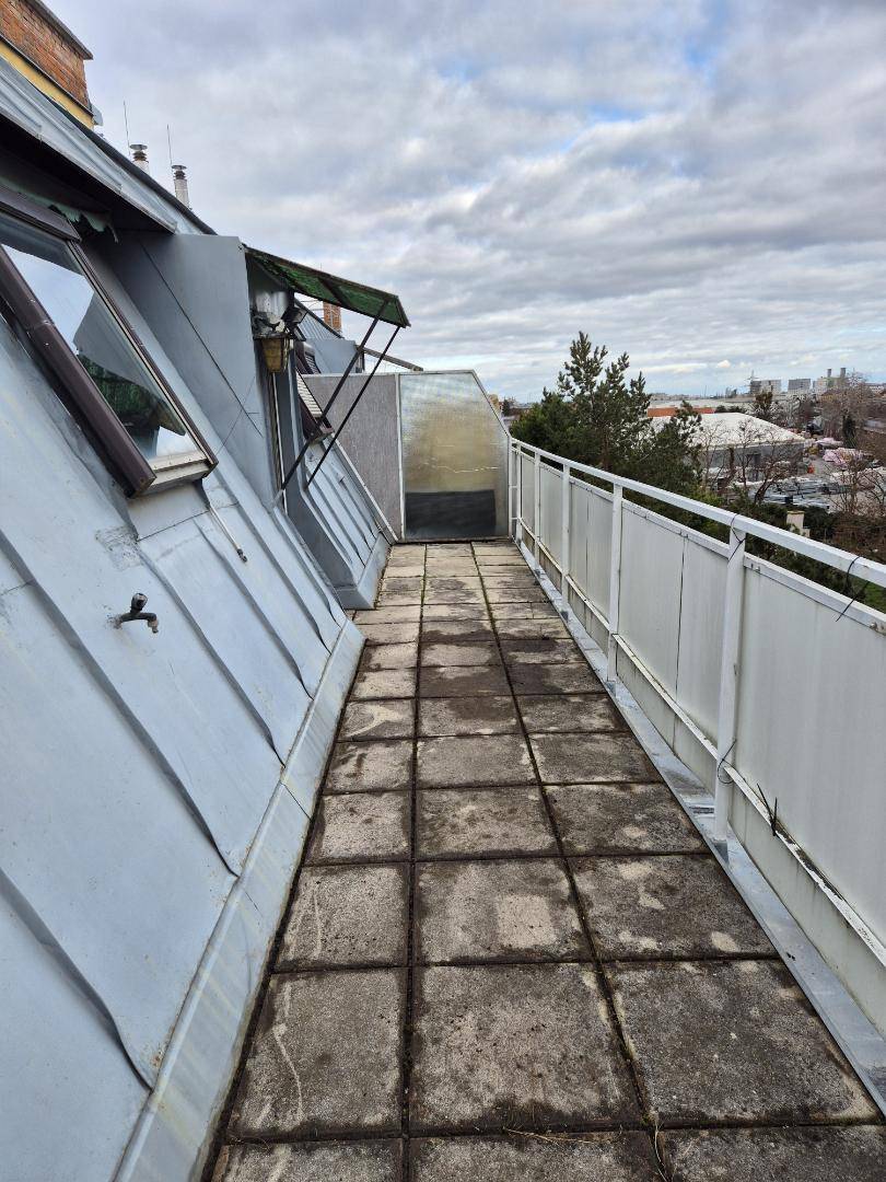 Schmaler Balkon mit alten Fliesen und schräger Dachkonstruktion, bietet einen Blick in die Ferne.
