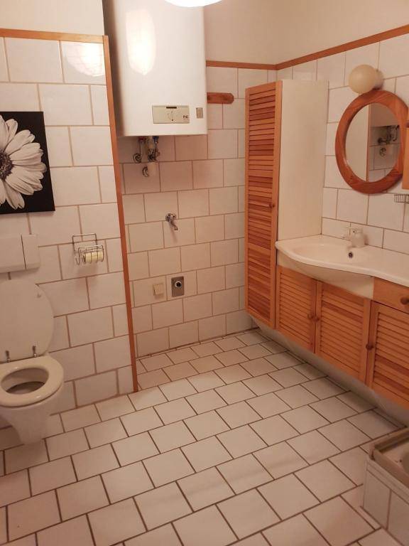 Badezimmer mit weißen Fliesen, WC, Waschbecken mit Holzunterschrank und rundem Spiegel.