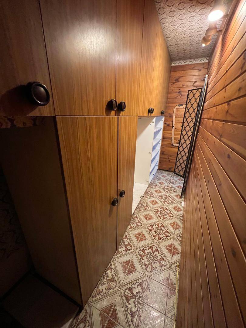 Langer Flur mit durchgehenden Holzschränken und rustikaler Holzvertäfelung an der Wand. Der Boden ist mit gemusterten Fliesen ausgelegt.