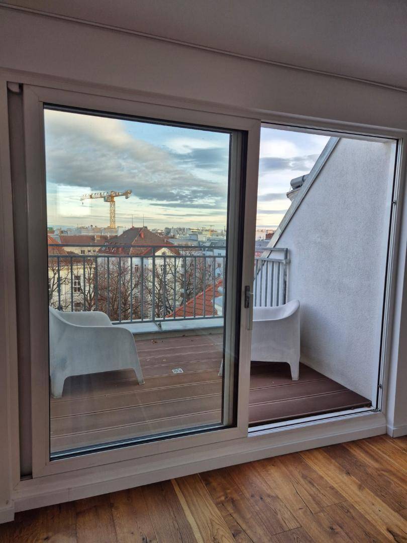 Blick vom Innenraum auf den Balkon mit Holzboden und Stadtpanorama.